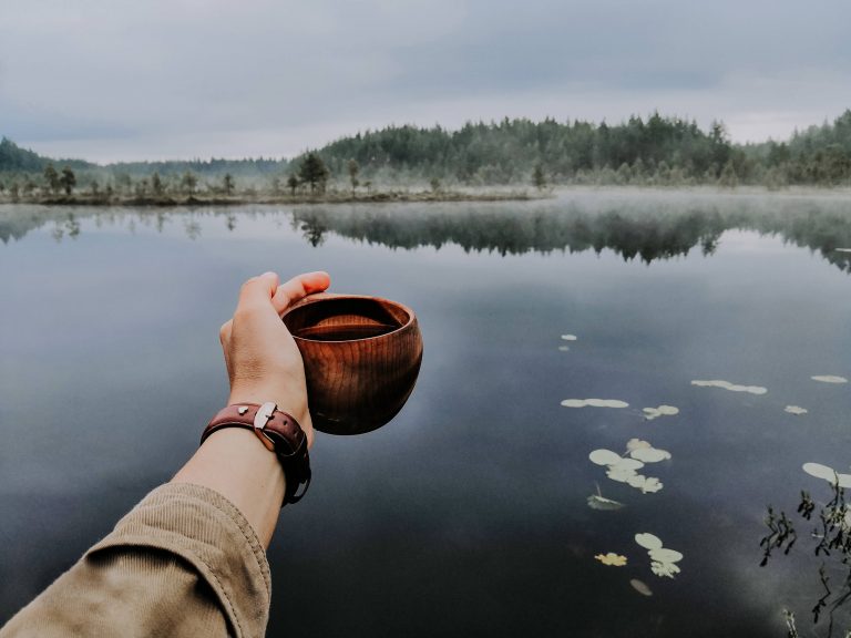 Hand held out holding cup by a lake