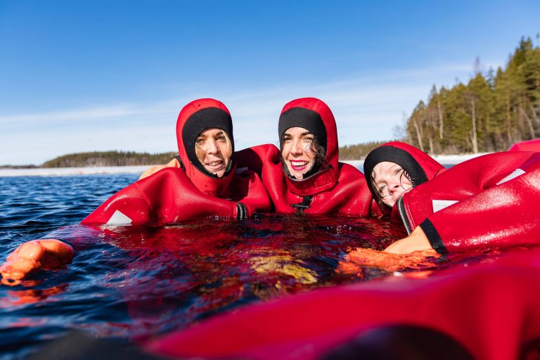Three people floating in the sea wearing red wetsuits 