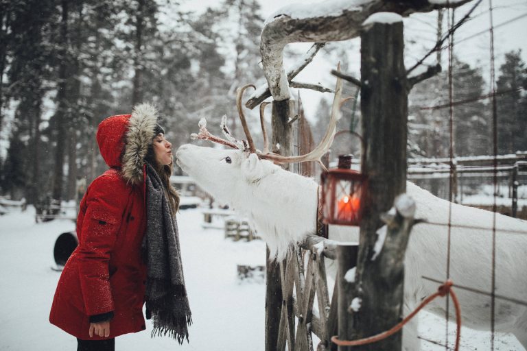 A woman wearing a red jacket kissing a reindeer on the mouth