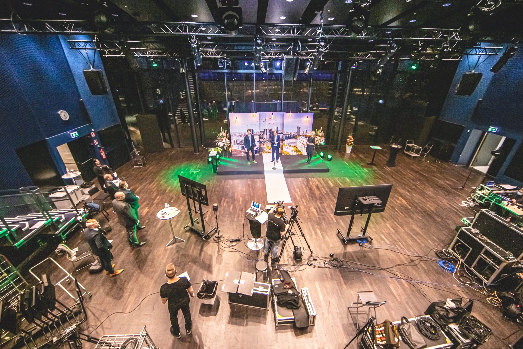 Birds eye view of people standing on a stage and film crew behind cameras and screens.
