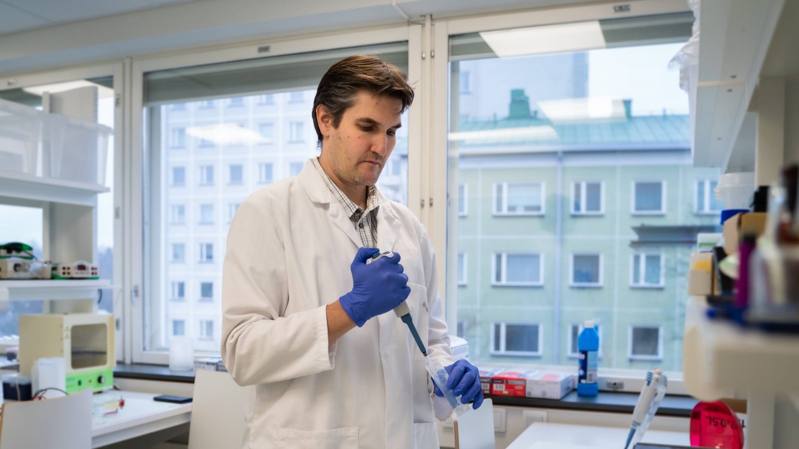 Man wearing a lab coat in a laboratory holding a pipette.