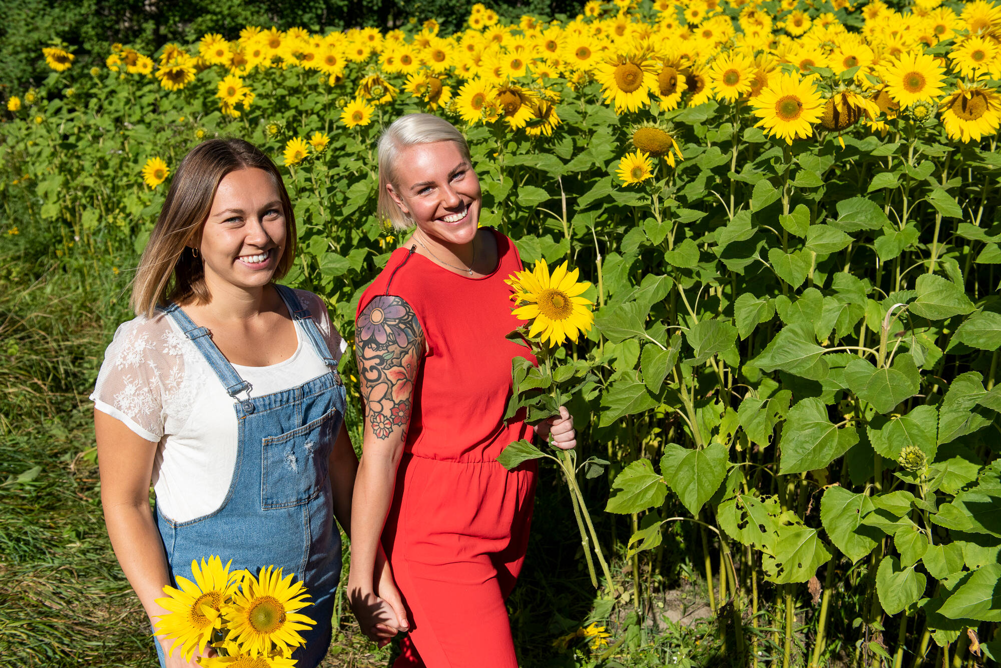 Two women standing by a sunflower field smiling at the camera.