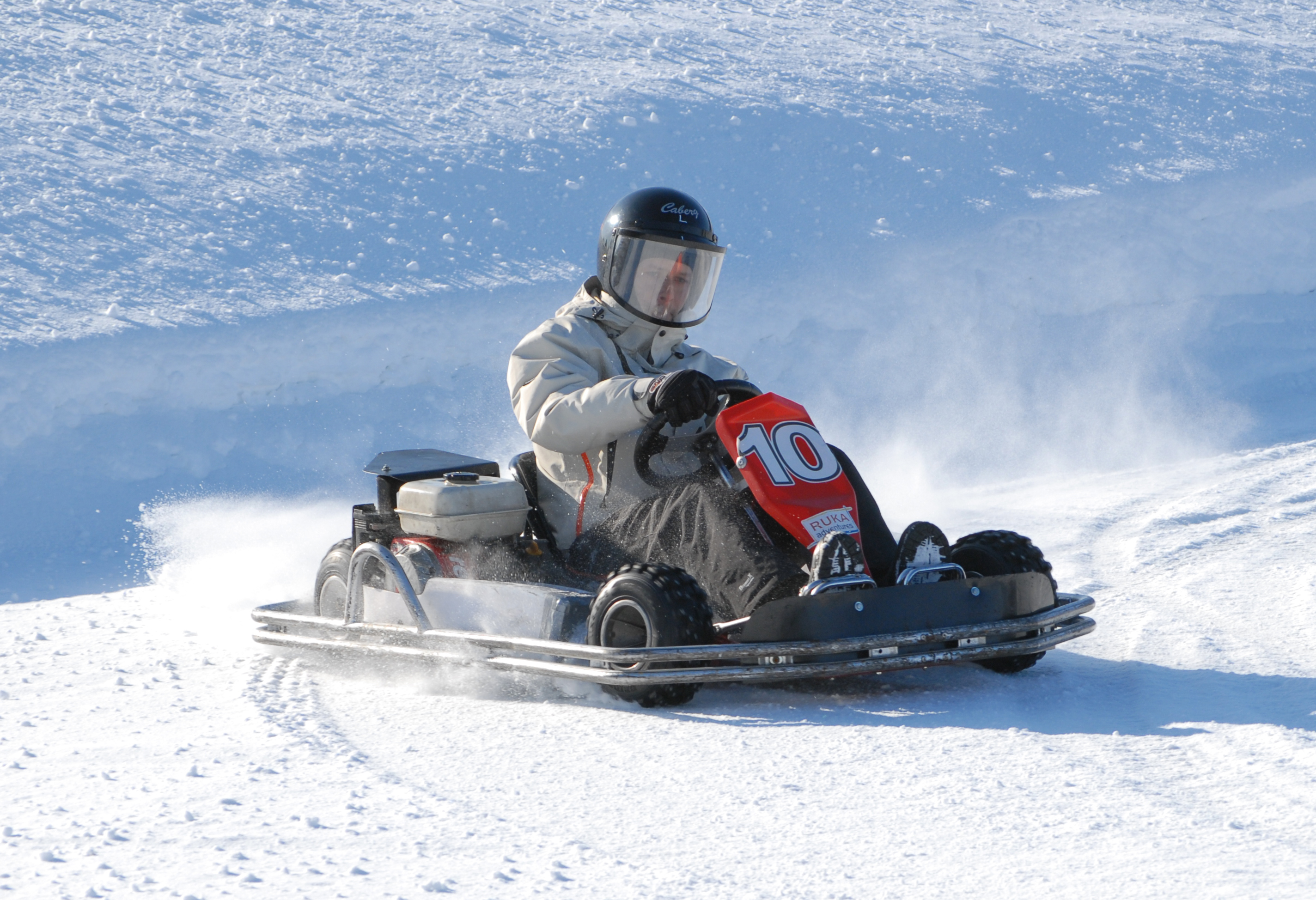 A person in a helmet and winter gear drives an ice kart labeled with the number 10.