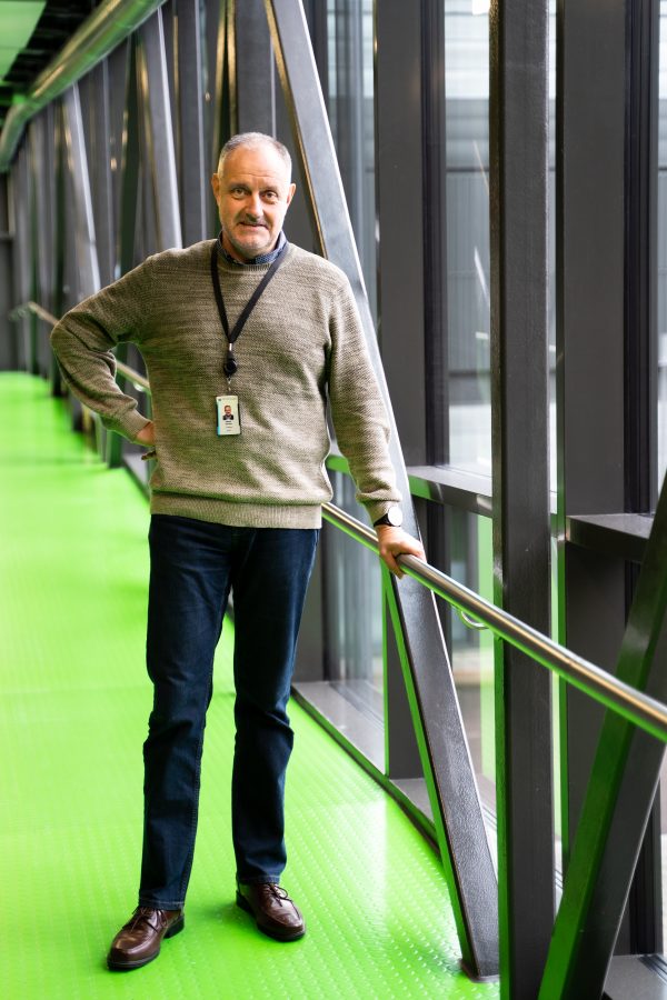Man holding a railing and looking at the camera in a venue with neon green floors.