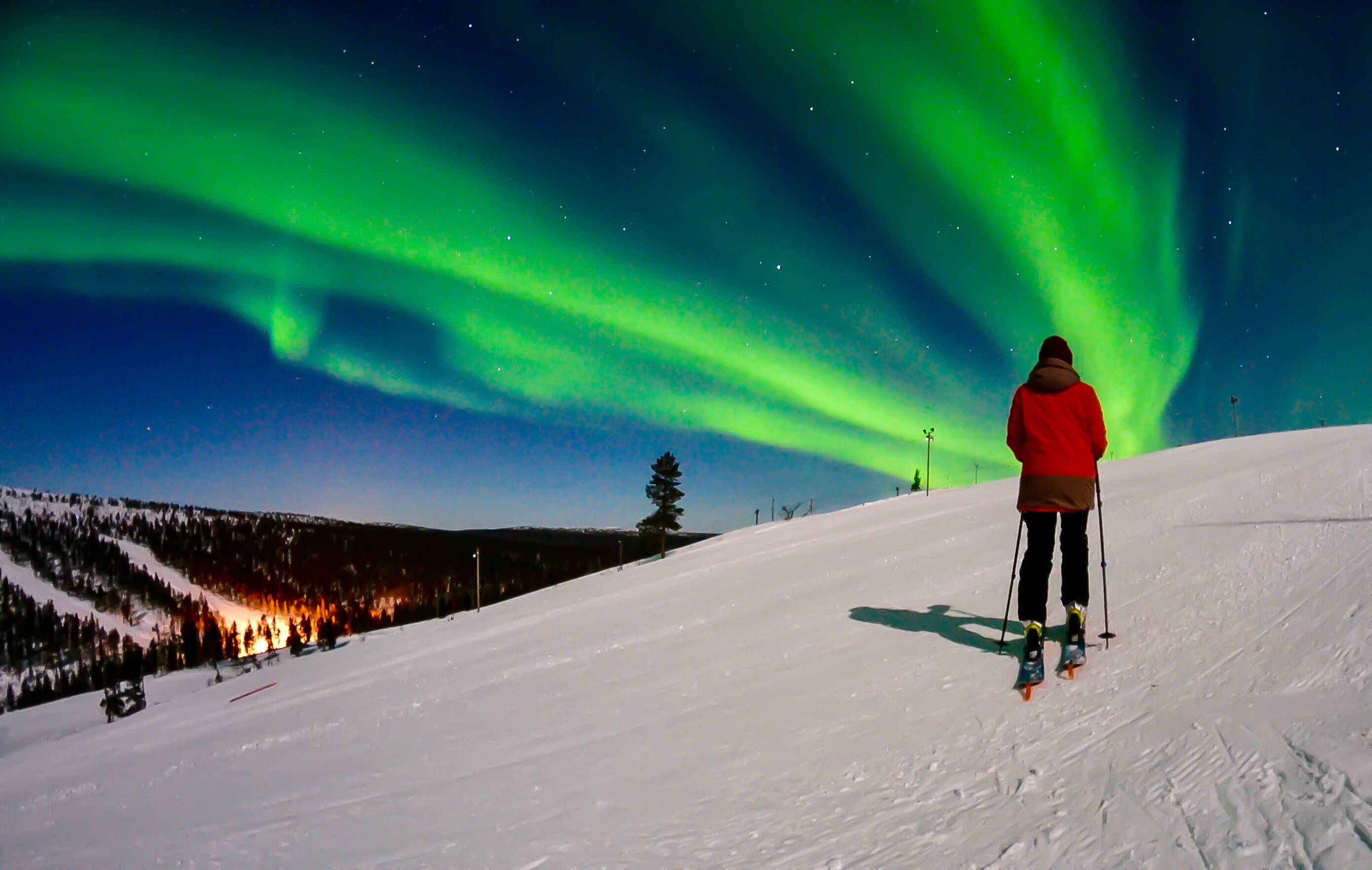 Skier staring at the Northern Lights above the ski slopes in Saariselkä, Finland.