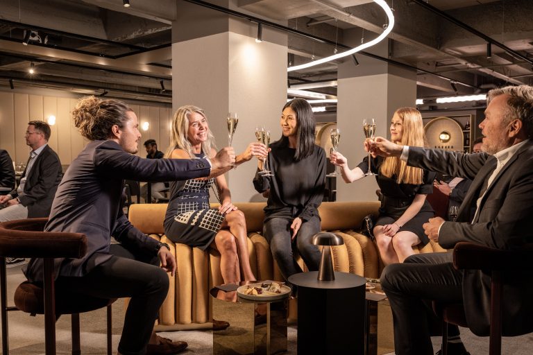 A group of people in business attire raise glasses of champagne to toast one another inside the new Helsinger event venue.