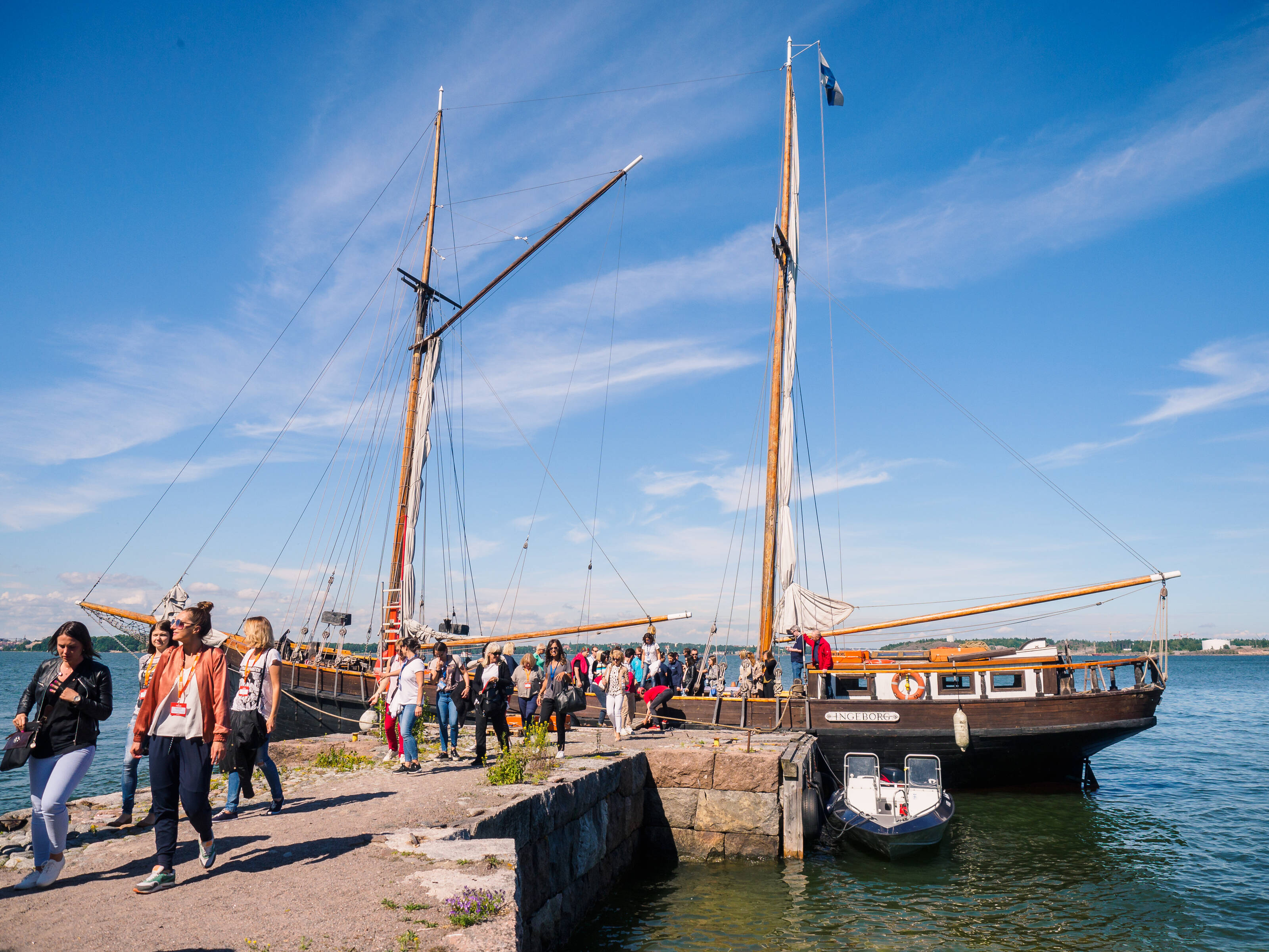 People on a pier in front of a wooden sailing ship