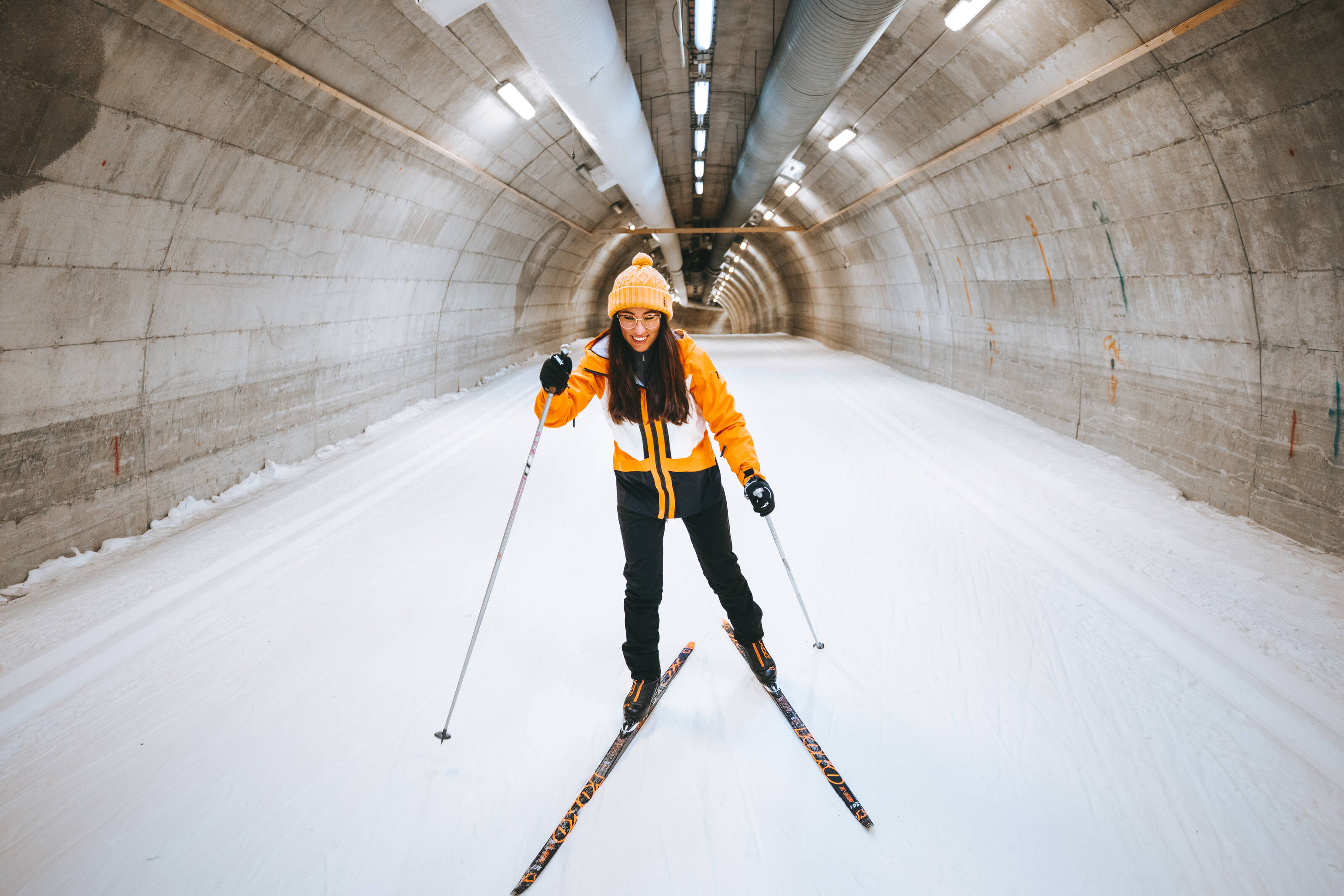 A happy woman in a yellow ski suit skiing in a tunnel.