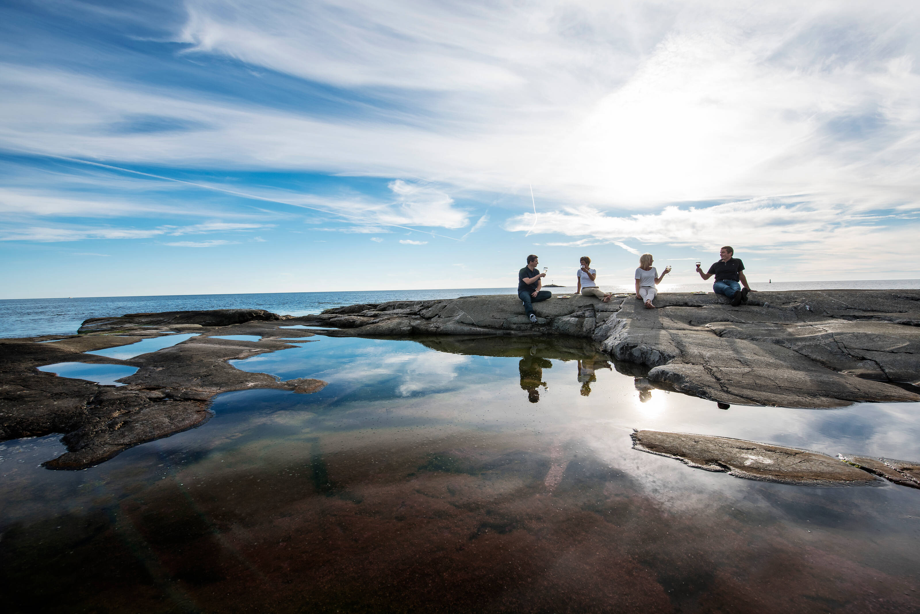 A group of friends sitting in the distance on top of cliffs by the sea on a sunny day in the archipelago.