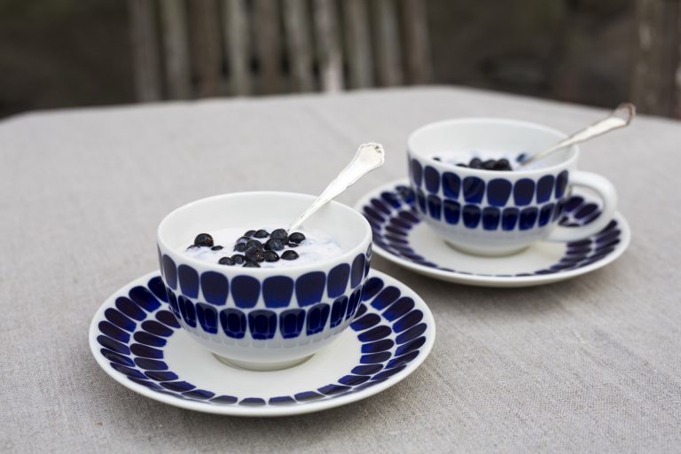 Two coffee cups with blue detailing containing yogurt and blueberries.