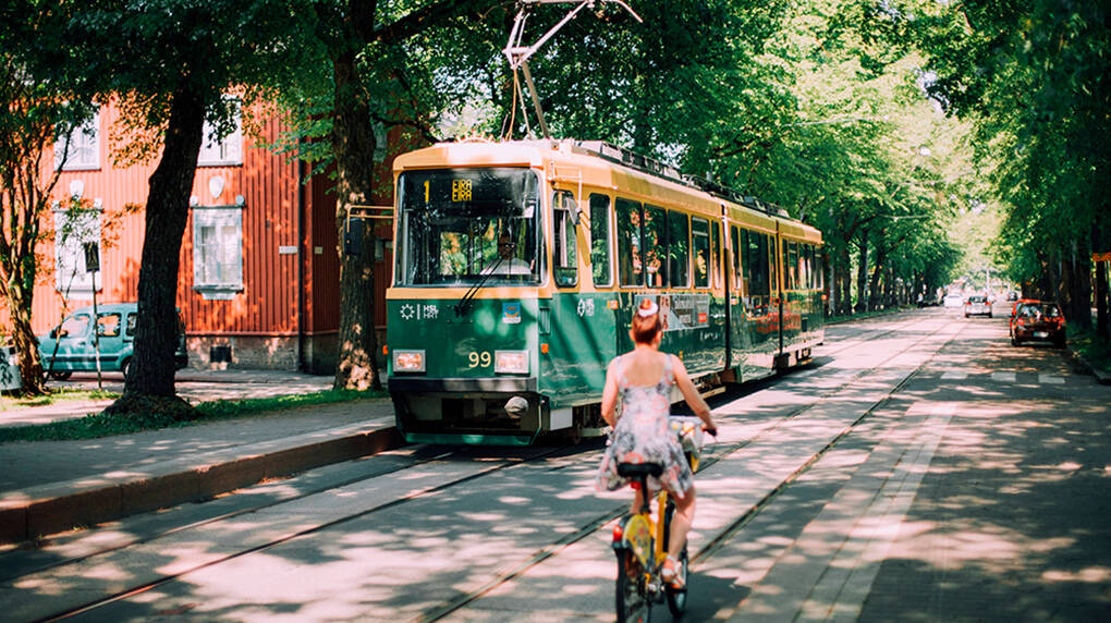 Woman biking on a sunny summer day whilst the tram is driving by in Helsinki, Finland