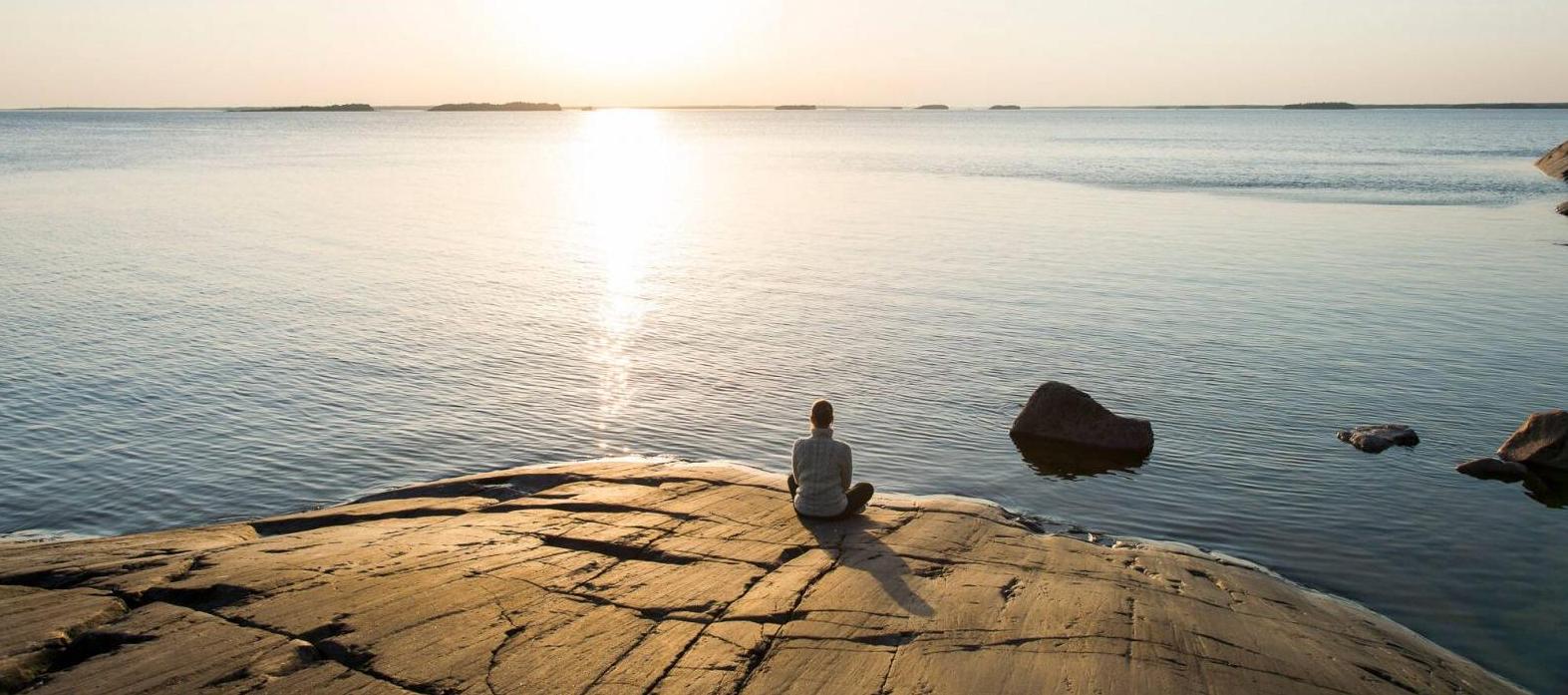 Person sitting on the cliff by the water watching the sunrise