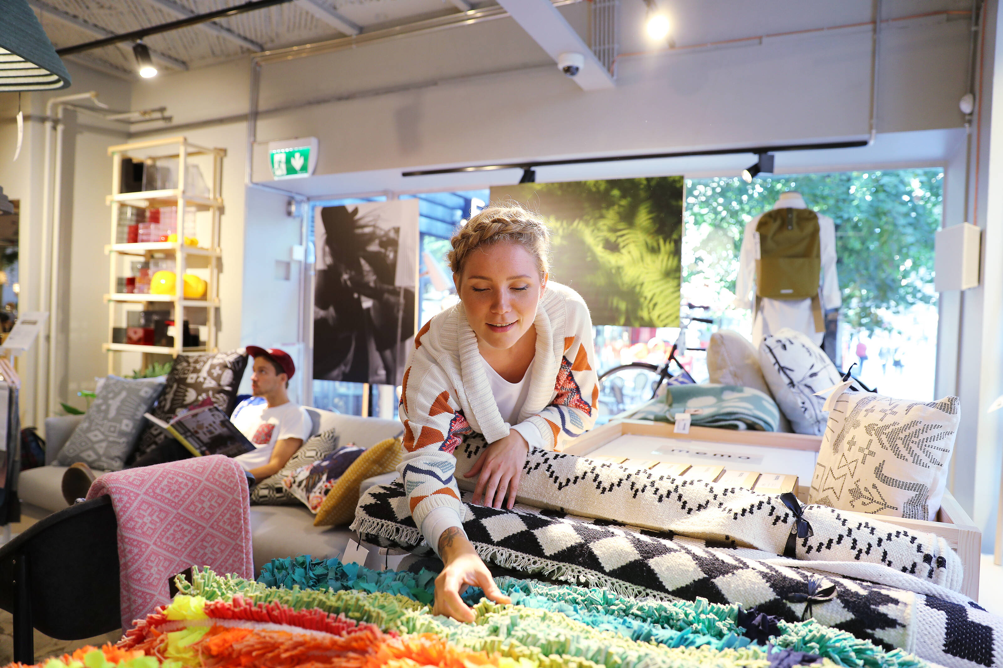 A woman with a braid in her hair inspects colourful textiles inside a design store.