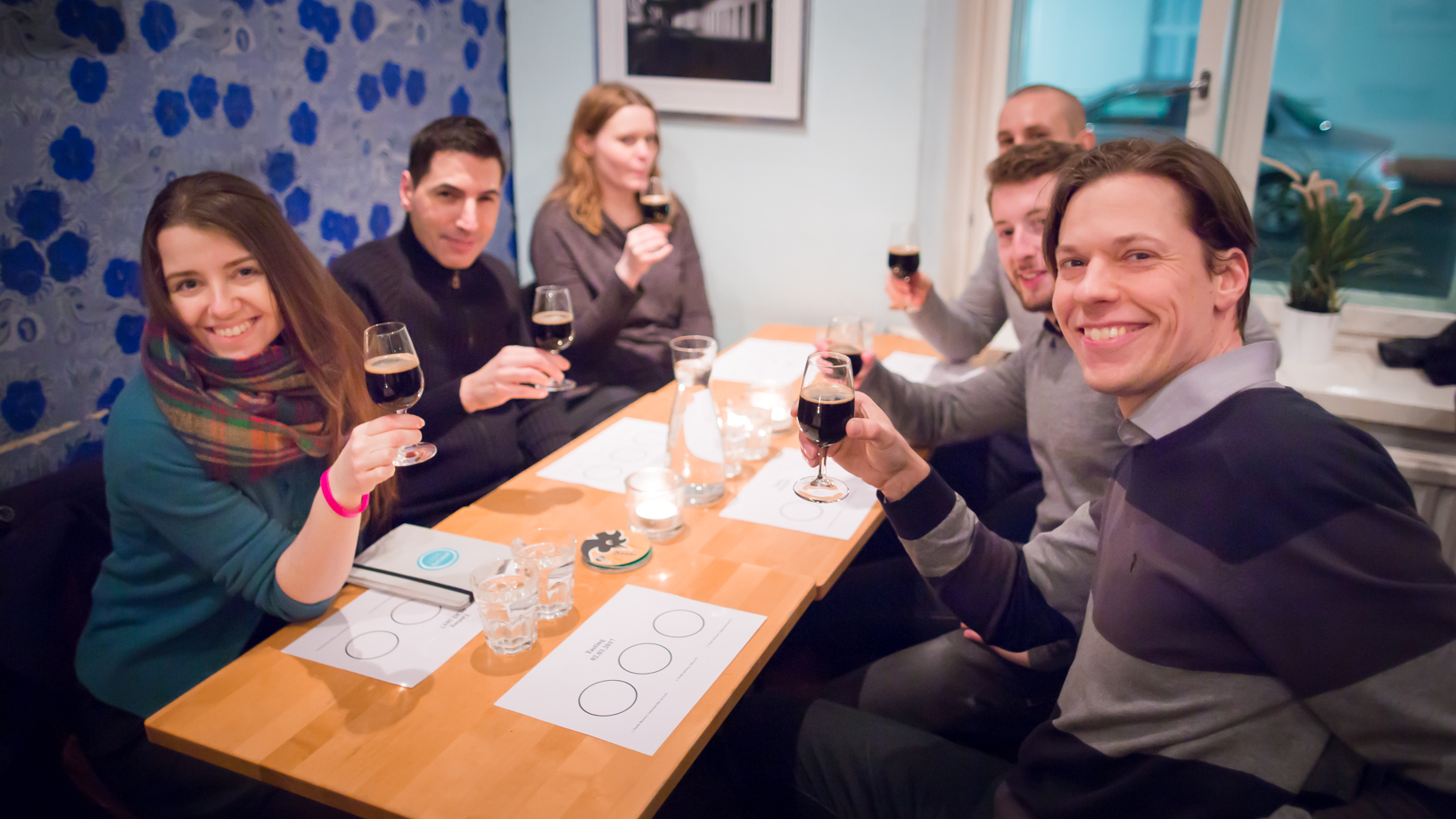 Six smiling people lift their glasses to share a toast inside a Finnish brewery.