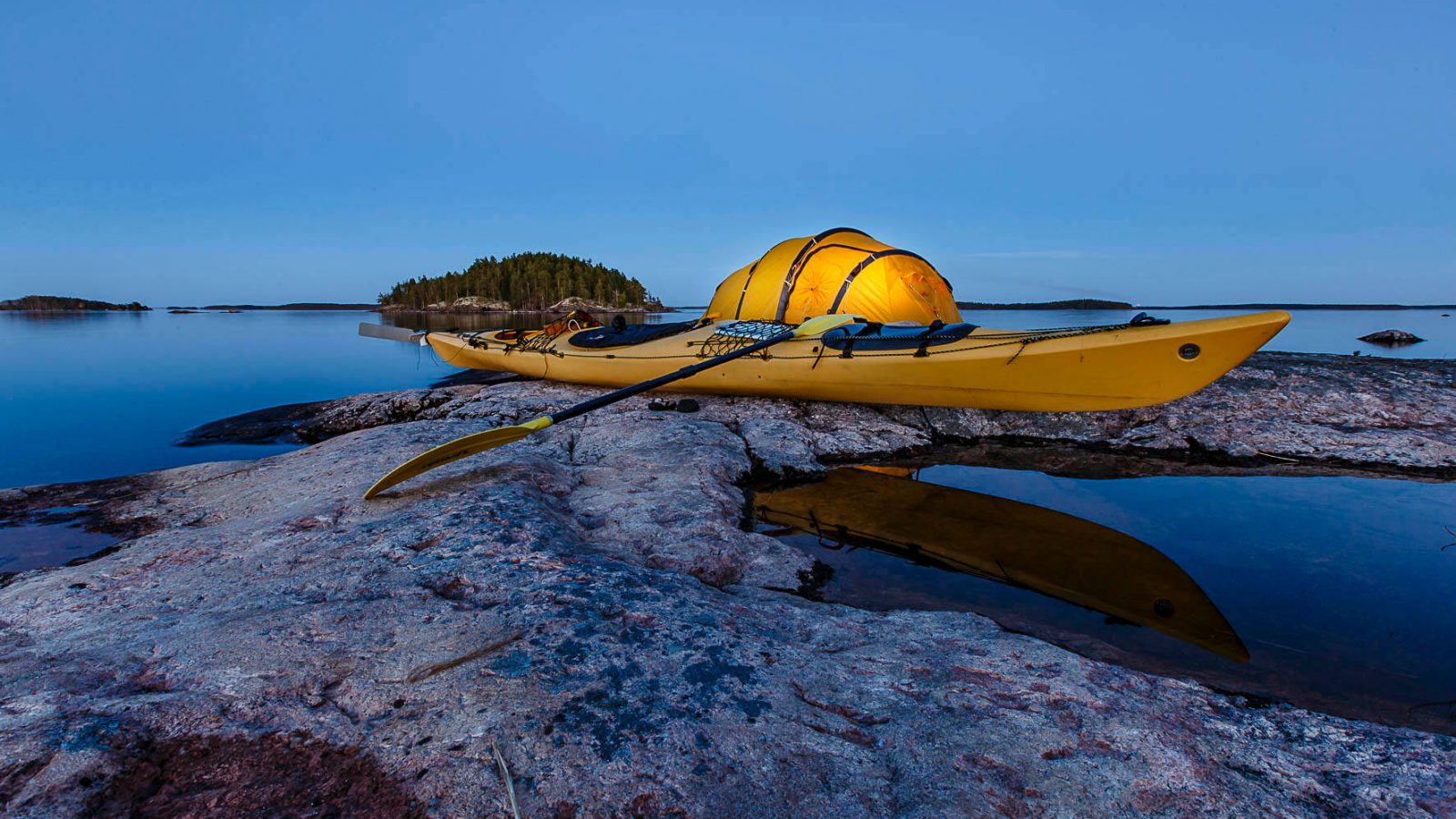 A yellow kayak and yellow tent on a cliff by the lake during nightfall